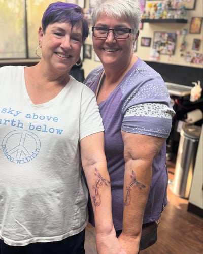 Matching delicate black and grey dragonfly tattoos on the forearm with fine line details — by Sandra Price, los angeles