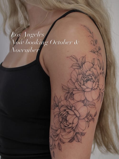A delicate black and grey fine line floral tattoo on the upper arm featuring detailed flowers and leaves — by Melanie Benoit, los angeles