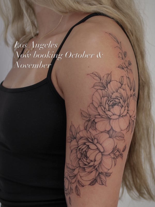A delicate black and grey fine line floral tattoo on the upper arm featuring detailed flowers and leaves — by Melanie Benoit, los angeles