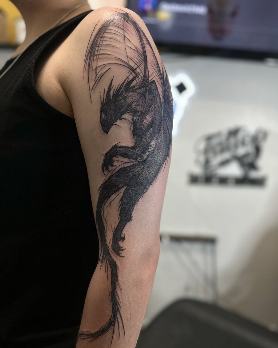 A bold black and grey sketch style dragon tattoo on the upper arm — by Maddie Ramirez, los angeles