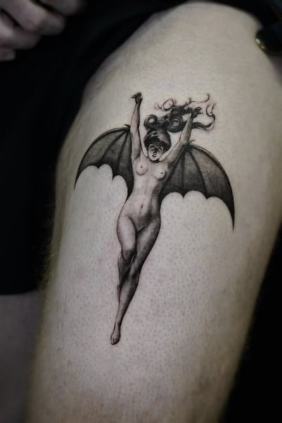 A black and grey surrealistic tattoo of a winged demon woman on the thigh, featuring detailed shading and a dynamic pose — by Jian Liang, los angeles