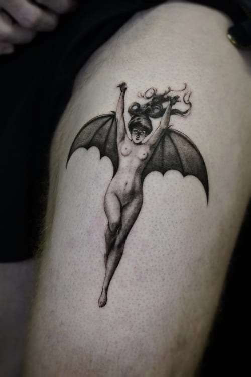 A black and grey surrealistic tattoo of a winged demon woman on the thigh, featuring detailed shading and a dynamic pose — by Jian Liang, los angeles