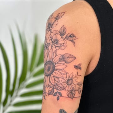A delicate black and grey floral tattoo featuring a sunflower on the upper arm, done in fine line style — by Melanie Benoit, los angeles
