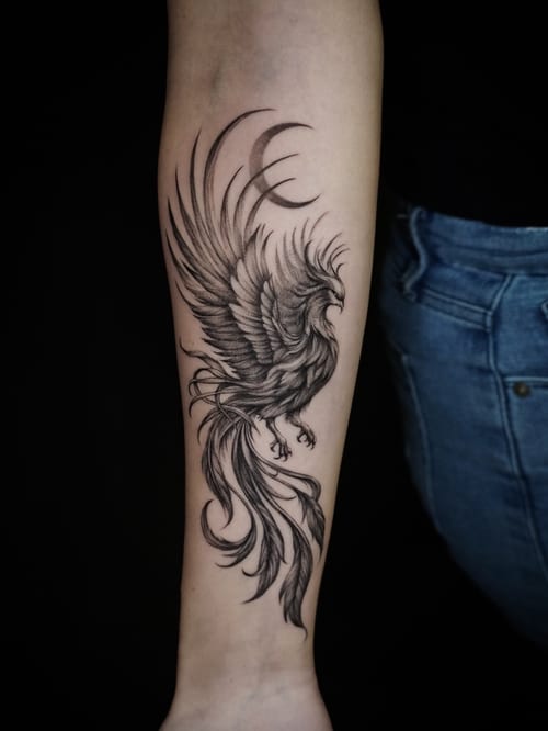 A detailed black and grey phoenix tattoo on the forearm, featuring intricate linework and shading to create a dynamic and elegant appearance — by Jian Liang, los angeles