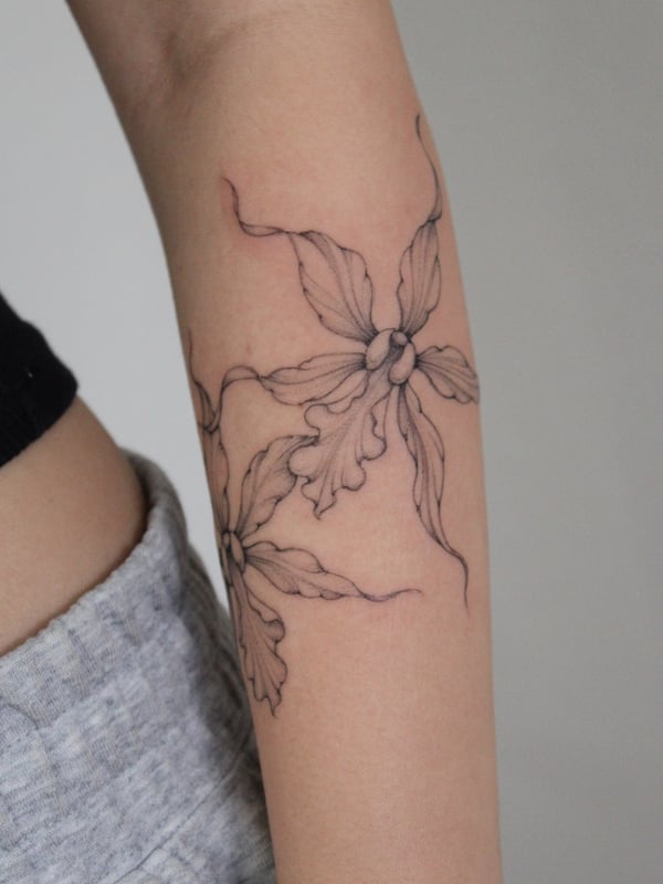 A delicate black and grey fine line floral tattoo on the forearm, featuring intricate flower designs — by Melanie Benoit, los angeles