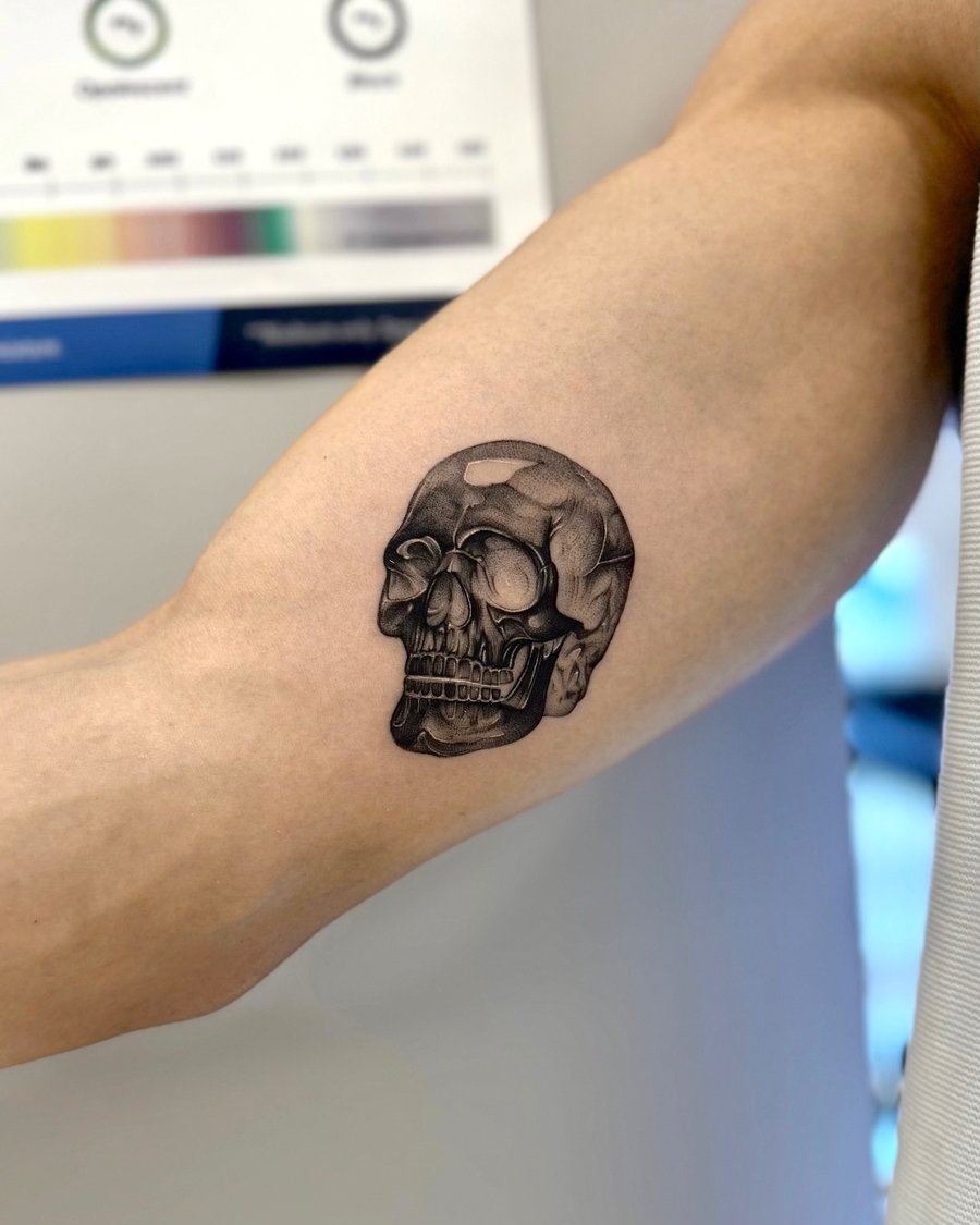 A detailed black and grey realism tattoo of a skull on the inner arm, showcasing intricate shading and depth — by otaybeatdown, los angeles