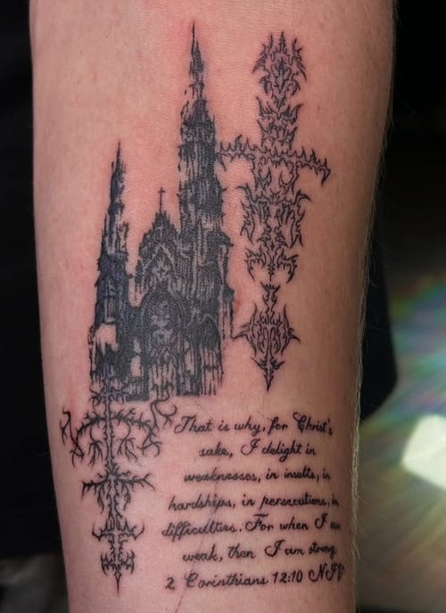 A black and grey tattoo on the forearm featuring a detailed gothic cathedral with intricate script below, conveying a religious theme — by NJ TATTOOZ, los angeles