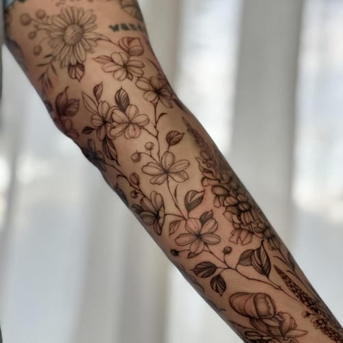 A delicate black and grey floral arrangement tattoo on the forearm, featuring fine line work and detailed botanical elements — by Melanie Benoit, los angeles