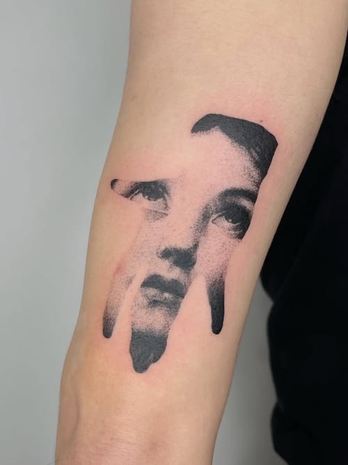 A black and grey portrait tattoo on the forearm, featuring a stylized face with bold blackwork elements — by Level tattoo, los angeles