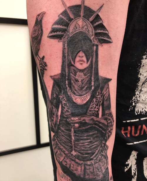 A dark and detailed black and grey tattoo of a mysterious figure with a raven on the forearm, featuring ornate headgear and intricate shading — by Sandra Price, los angeles
