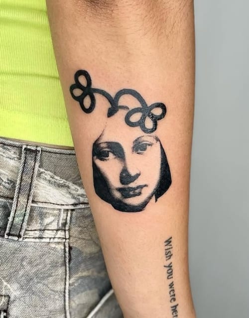 A black and grey surrealist portrait tattoo on the forearm, featuring a stylized face with abstract elements — by Level tattoo, los angeles