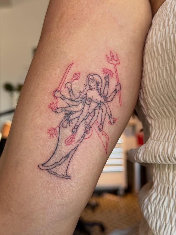 A minimalist linework tattoo of a multi-armed goddess on the arm, featuring delicate and spiritual elements with mixed color highlights — by Kiera Garvin, los angeles