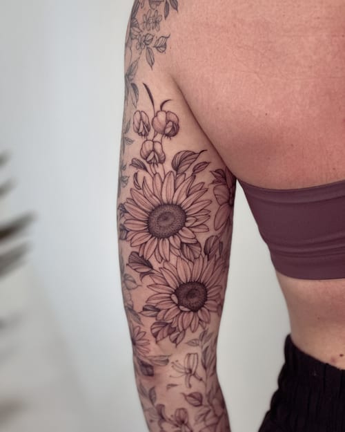 A delicate black and grey floral tattoo featuring sunflowers on the arm, showcasing intricate botanical details — by Melanie Benoit, los angeles