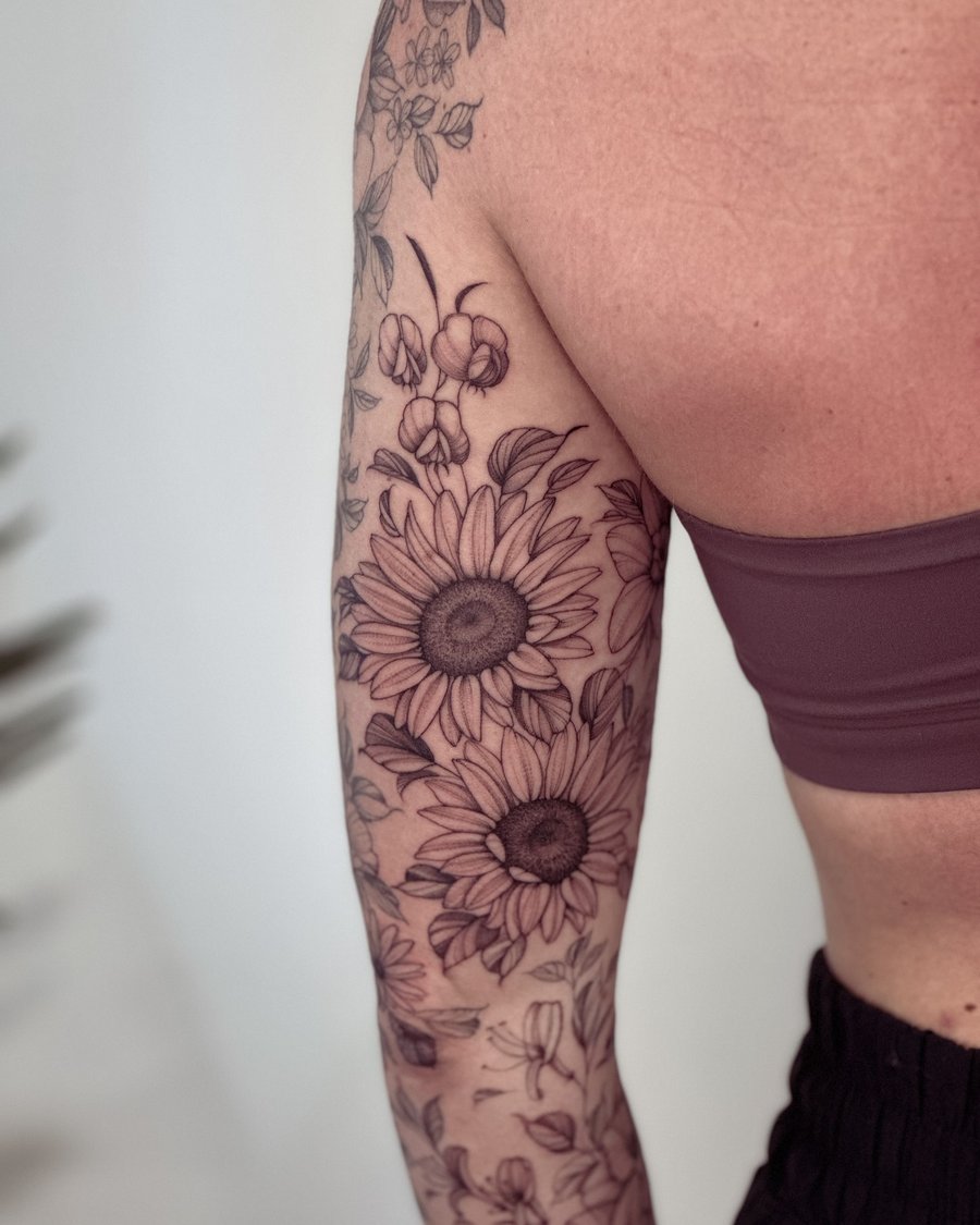 A delicate black and grey floral tattoo featuring sunflowers on the arm, showcasing intricate botanical details — by Melanie Benoit, los angeles