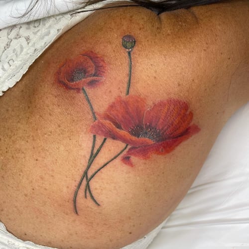 A realistic color tattoo of poppies on the back, featuring delicate floral details and vibrant red hues — by Sandra Price, los angeles