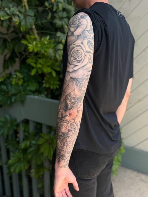 A detailed black and grey rose bouquet tattoo covering the full sleeve with realistic shading and intricate floral design — by Sandra Price, los angeles