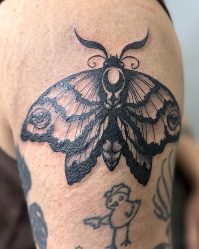A bold blackwork moth tattoo on the upper arm with fine line details — by Maddie Ramirez, los angeles