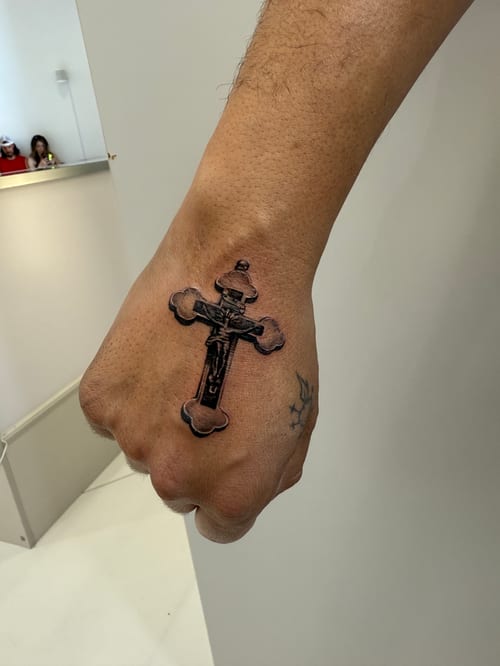 A black and grey realistic cross tattoo on the hand with detailed shading and texture — by 钟逸政, los angeles