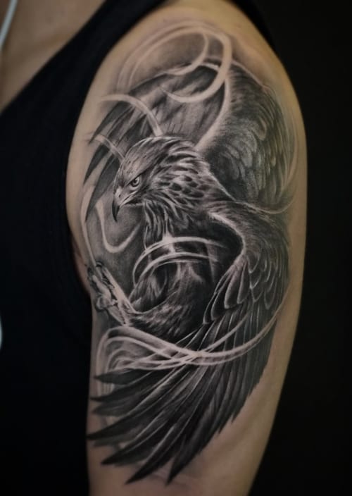 A detailed black and grey realism tattoo of an eagle with outstretched wings on the upper arm, featuring intricate shading and dynamic lines — by Jian Liang, los angeles