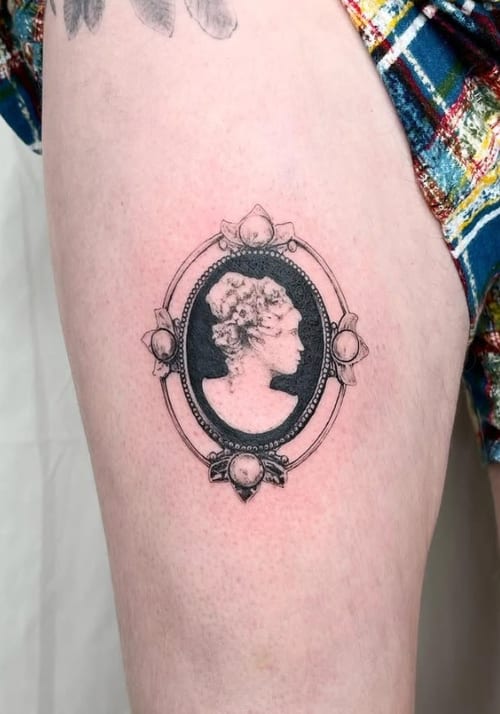 A black and grey fine line cameo-style portrait on the thigh, featuring intricate detailing within an ornate frame — by Level tattoo, los angeles