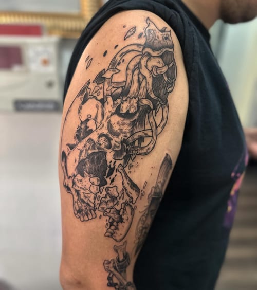 An abstract blackwork tattoo of a skull with mechanical elements on the upper arm — by Maddie Ramirez, los angeles