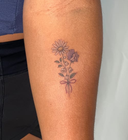 A delicate fine line flower bouquet tattoo on the forearm, featuring colorful flowers tied with a ribbon — by Melanie Benoit, los angeles