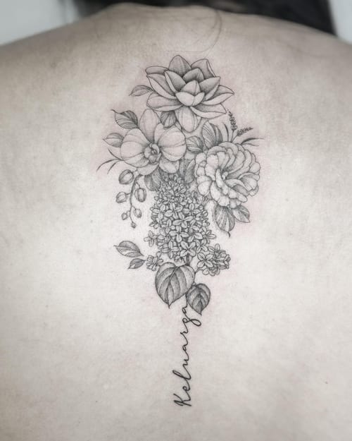 A delicate black and grey floral bouquet tattoo on the back with fine line details and script lettering — by Melanie Benoit, los angeles