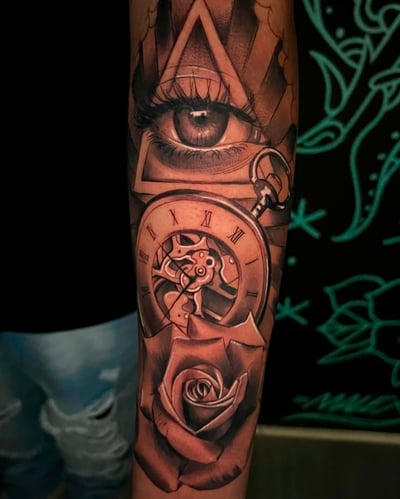 A detailed black and grey tattoo on the forearm featuring a realistic eye, a clock with Roman numerals, and a rose, all enclosed within geometric shapes — by Josue Bravo, los angeles