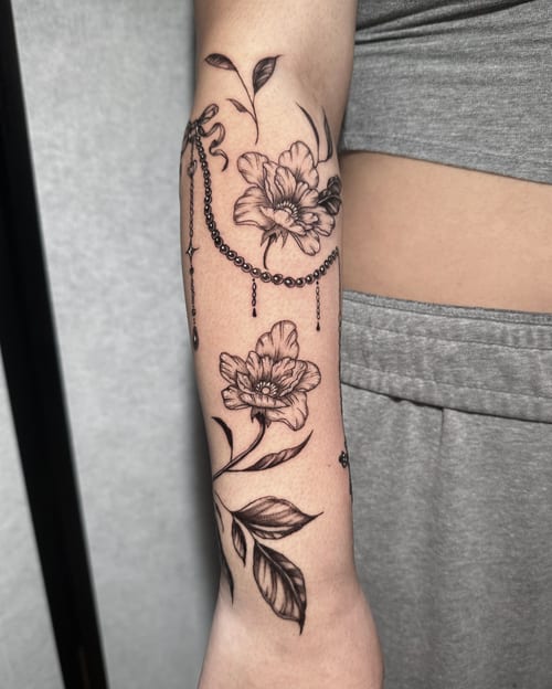 A fine line black and grey floral tattoo on the forearm, featuring delicate flowers and leaves with intricate details — by Shelby Bianco, los angeles