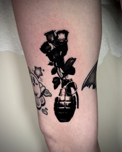 A blackwork tattoo of roses growing out of a grenade on the thigh, featuring bold black ink and illustrative style — by emily, los angeles