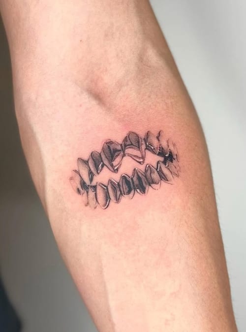 A black and grey tattoo of a set of teeth on the forearm, featuring bold linework and shading — by Level tattoo, los angeles