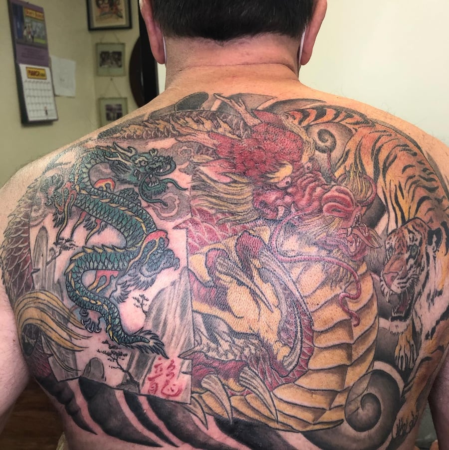 A colorful Japanese-style tattoo featuring a dragon and tiger on the back, showcasing bold and ornate designs — by Sandra Price, los angeles