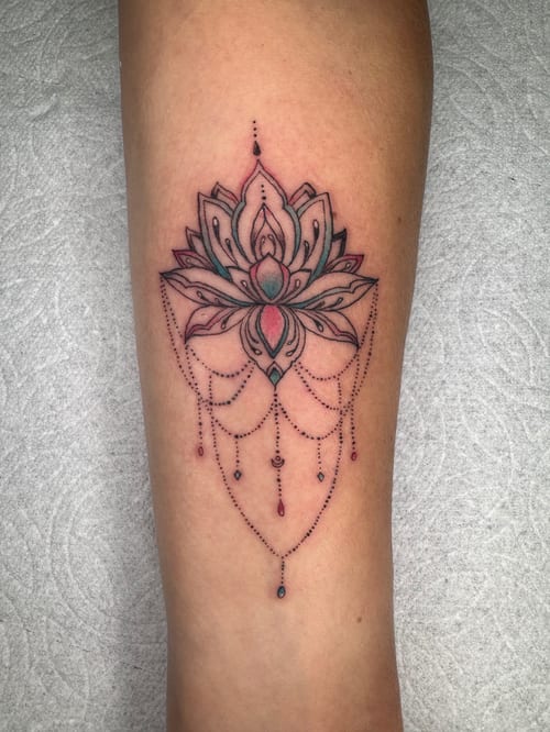 A delicate ornamental lotus flower tattoo on the forearm with dotwork details and subtle color accents — by Sandra Price, los angeles