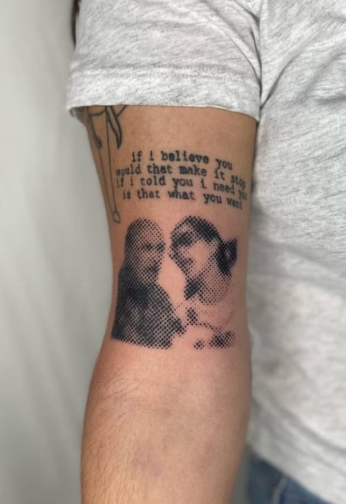 A black and grey dotwork tattoo on the upper arm featuring two portraits and a quote above them — by Level tattoo, los angeles