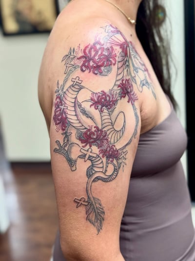 A bold dragon tattoo with red flowers on the upper arm, featuring a mix of black and red ink in a Japanese style — by Sandra Price, los angeles