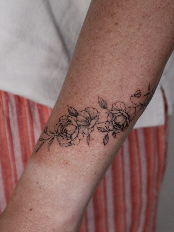 A delicate black and grey floral band tattoo on the forearm, featuring fine line flowers and leaves — by Melanie Benoit, los angeles