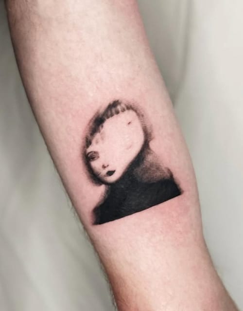 A surreal black and grey portrait on the forearm, featuring a distorted face with soft shading and abstract elements — by Level tattoo, los angeles