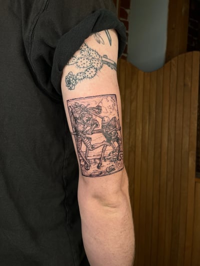 A black and grey tattoo of skeletons fighting with swords on the upper arm, featuring detailed linework and a dark, graphic style — by Dylan Aiello, los angeles
