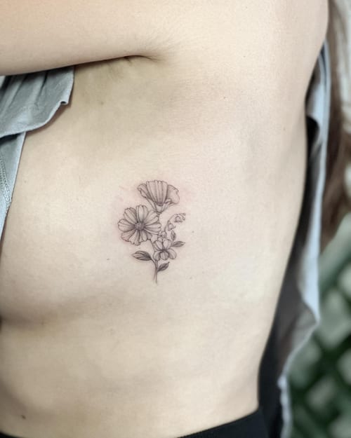 A delicate black and grey fine line flower bouquet tattoo on the rib, featuring minimalist floral design — by Melanie Benoit, los angeles