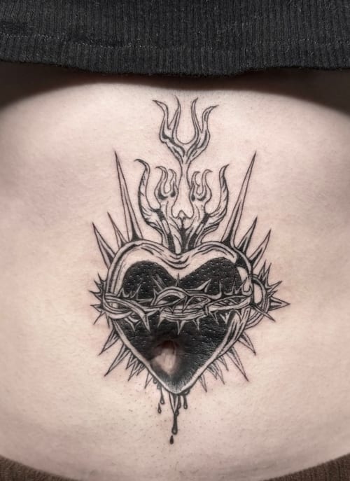 A black and grey tattoo of a heart with thorns and flames on the stomach, featuring bold linework and intricate details — by Shelby Bianco, los angeles