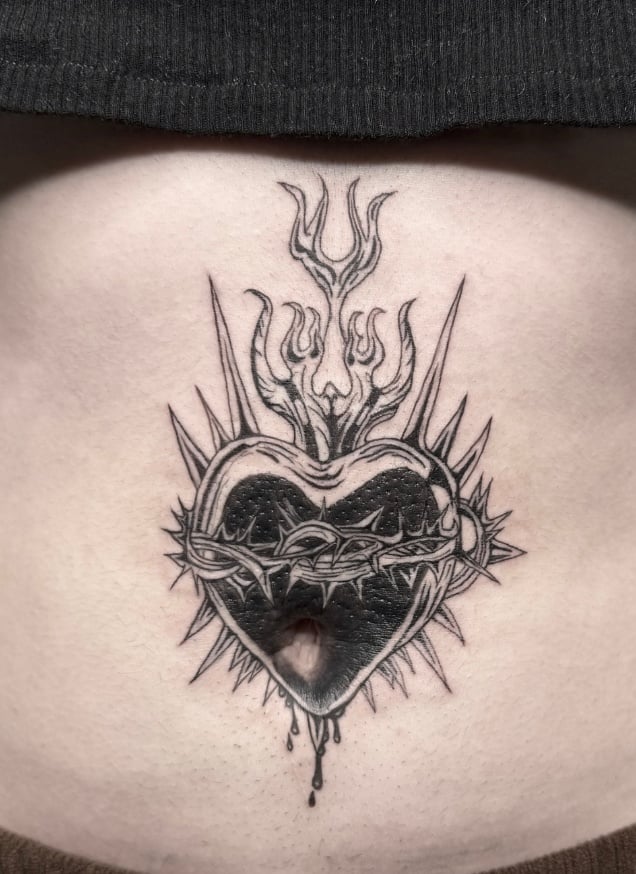 A black and grey tattoo of a heart with thorns and flames on the stomach, featuring bold linework and intricate details — by Shelby Bianco, los angeles