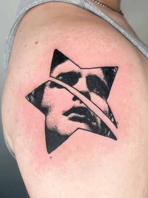 A black and grey abstract tattoo of a face within a star shape on the shoulder, featuring bold blackwork lines and shading — by Level tattoo, los angeles