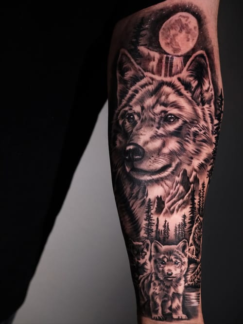 A detailed black and grey wolf tattoo on the forearm, featuring a moon and forest background — by Johnny Ayala, los angeles