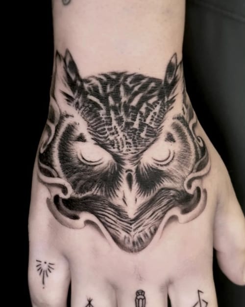 A black and grey blackwork tattoo of an owl on the hand, featuring bold lines and intricate shading — by Jian Liang, los angeles