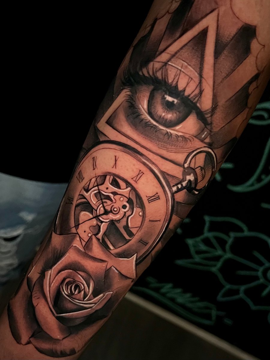 A realistic black and grey tattoo on the forearm featuring a detailed eye, a pocket watch with Roman numerals, and a rose, all intricately shaded — by Josue Bravo, los angeles