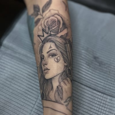 A delicate black and grey portrait of a woman with a crown and rose on the forearm — by Maddie Ramirez, los angeles