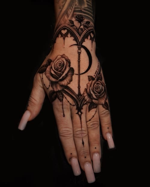 A black and grey tattoo on the hand featuring ornamental roses and a crescent moon with intricate detailing — by Vladimir Kozachenko, los angeles