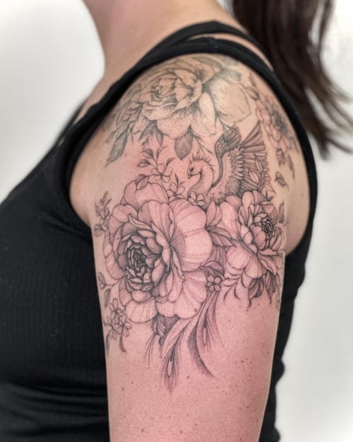A delicate black and grey tattoo of flowers and a bird on the shoulder, featuring intricate floral details — by Melanie Benoit, los angeles