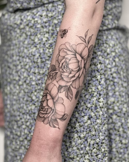 A delicate black and grey floral tattoo with a bee on the forearm, featuring fine line work and clean detailing — by Melanie Benoit, los angeles