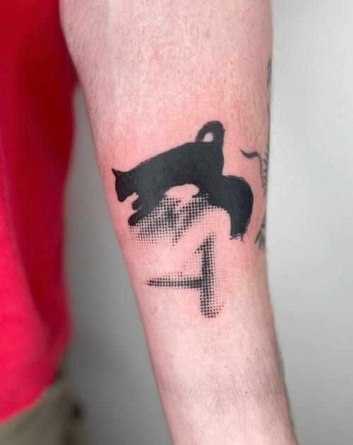 A black and grey tattoo on the forearm featuring a silhouette of a cat with dotwork shading below it — by Level tattoo, los angeles